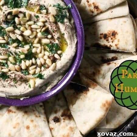 Party Hummus, the ultimate creamy dip, served with a garnish of olive oil, pine nuts, and parsley.