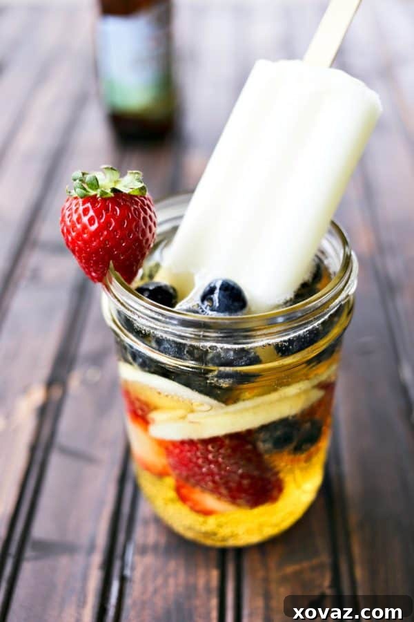 Hard Cider Sangria-by-the-Glass with vibrant fresh fruits submerged in a crisp apple cider, featuring a refreshing lime ice pop as a stir stick.