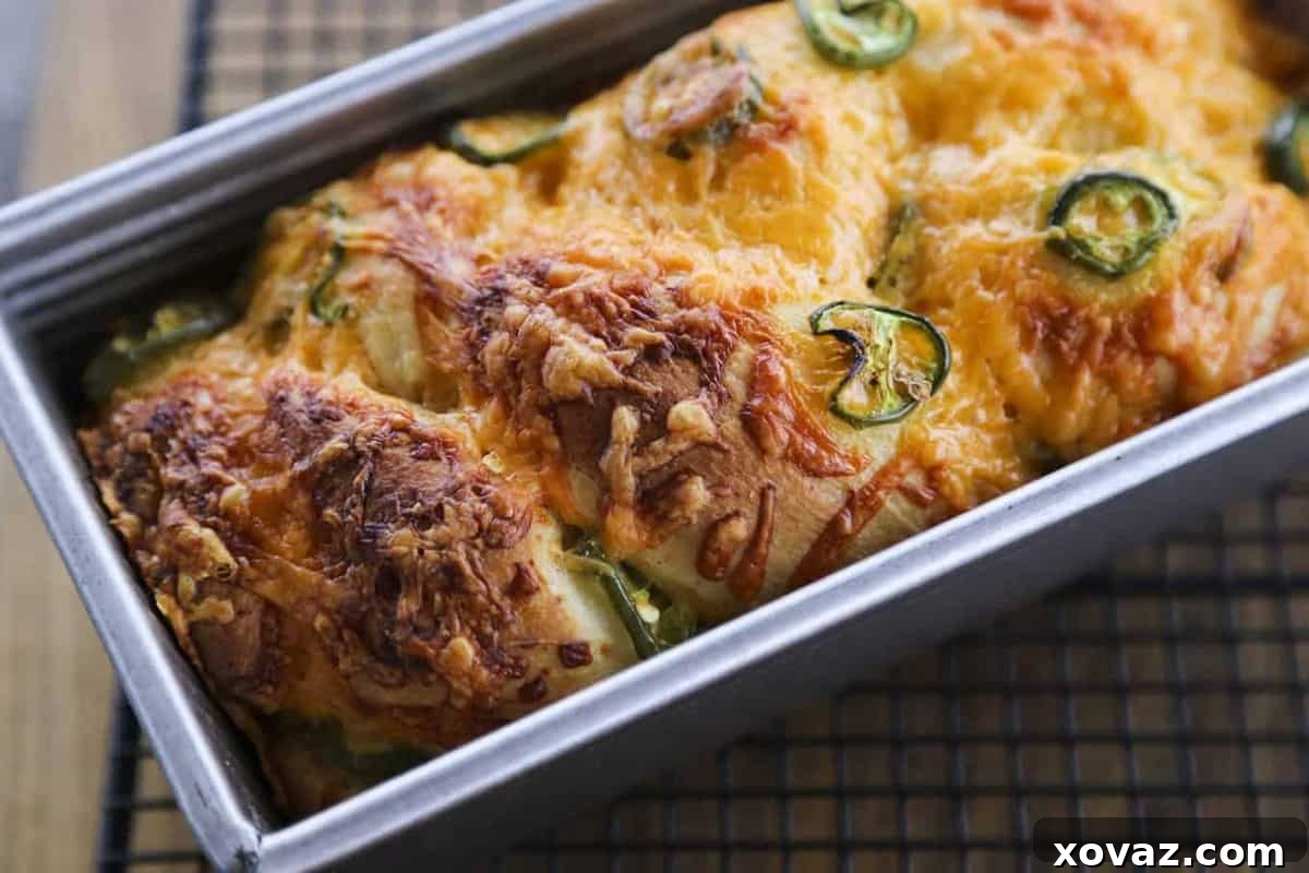 A close-up view of a baked Jalapeno Cheddar Bread loaf, showing the rich, golden-brown crust, visible slices of green jalapeno, and savory melted cheddar cheese throughout.