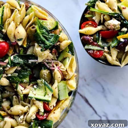 A vibrant bowl of Veggie Lover's Greek Pasta Salad, showcasing fresh spinach, cucumbers, tomatoes, bell peppers, Greek olives, and red onions with tender pasta, all dressed in a zesty lemon-herb dressing.