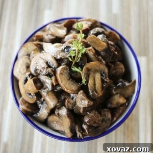 blue edged, white ceramic bowl, wooden tile background, simple garlic butter sauteed mushrooms, sprig of fresh thyme