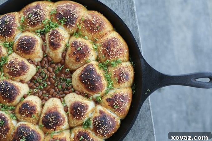 Cheeseburger Bombs Baked Bean Skillet is a whole host of comfort foods in one pan! Delicious rolls stuffed with melted Cheddar cheese and tender meatballs, baked in a cast iron skillet around barbecue baked beans. This is as good as game day food gets!