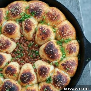 Cheeseburger Bombs Baked Bean Skillet, sesame topped rolls stuffed with meatballs, arranged in circles around baked beans, cast iron skillet, sliced green onions