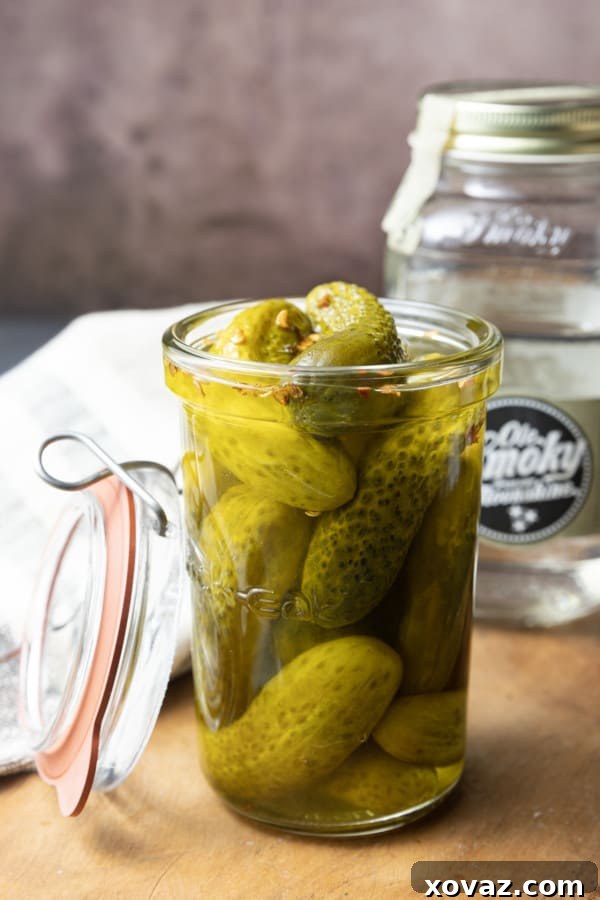 A jar of homemade Moonshine Pickles, showcasing their vibrant green color and the spicy red pepper flakes suspended in the brine. These high-octane pickles are perfect for snacking or as a unique cocktail ingredient, offering a delicious crunch and a spirited kick.