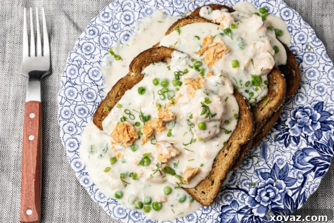 A bowl of creamy salmon with peas, served over buttered toast, garnished with fresh green herbs.