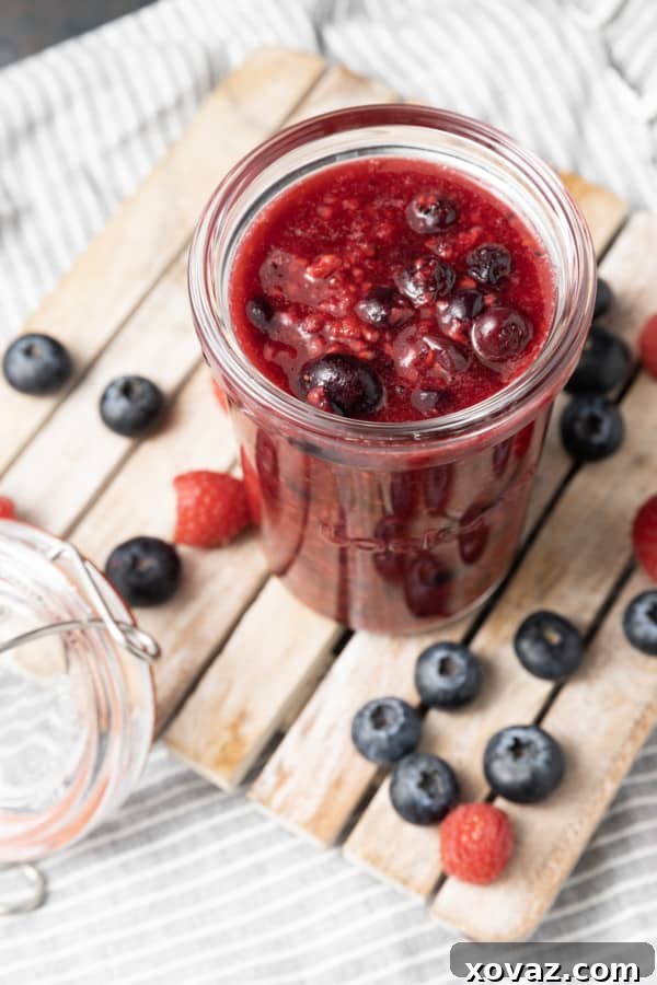 A spoonful of vibrant berry compote being drizzled over a dessert, showcasing its rich texture and natural fruit pieces.