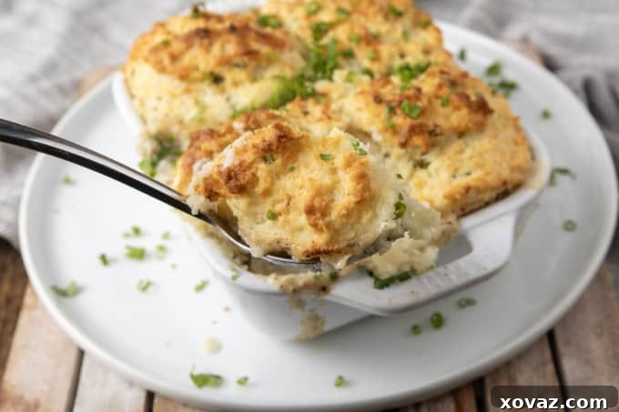 small white casserole dish filled with sausage gravy and topped with buttermilk biscuit crust on top of a plate with a spoon in it.