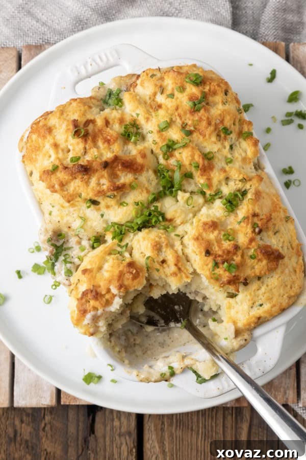small white casserole dish filled with sausage gravy and topped with buttermilk biscuit crust on top of a plate with a spoon in it.