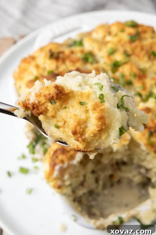 small white casserole dish filled with sausage gravy and topped with buttermilk biscuit crust on top of a plate with a spoon in it.