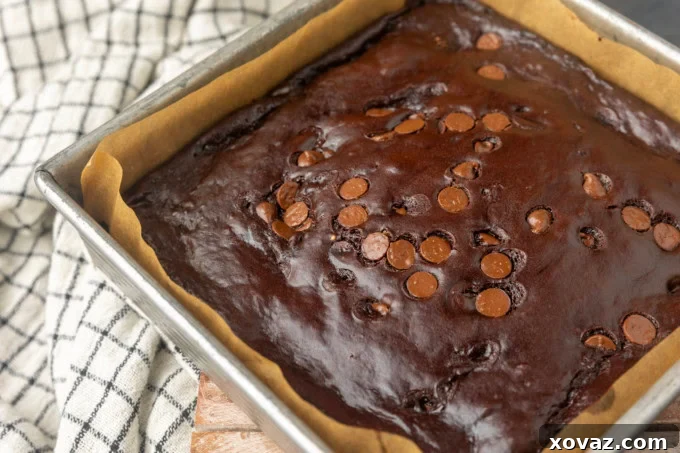 Freshly baked Greek yogurt brownies cooling in a pan lined with parchment paper, emphasizing the ease of removal and minimal cleanup for this eggless recipe.