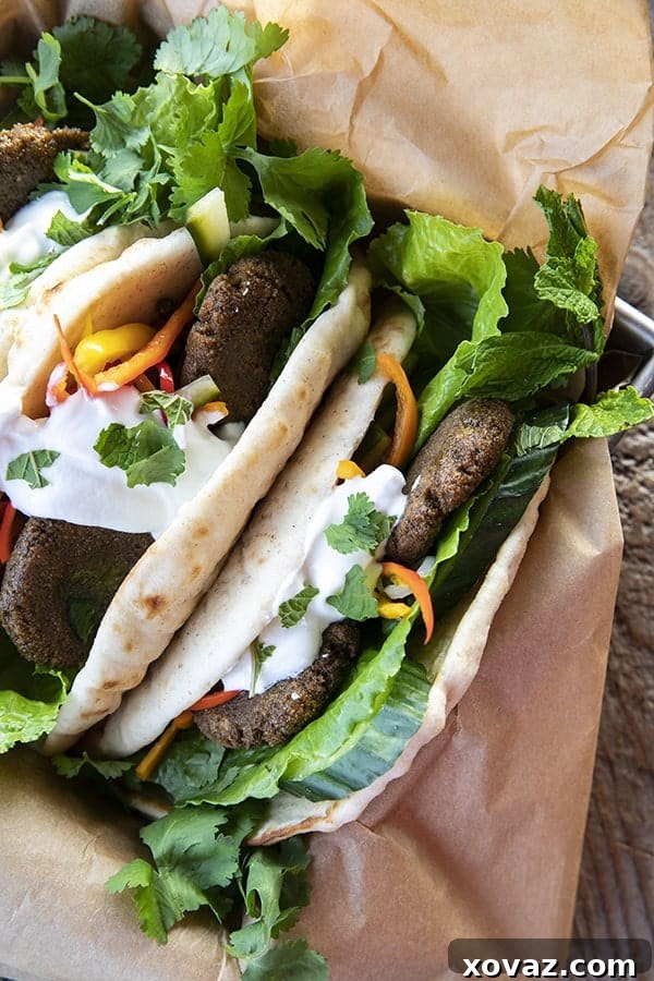 Top view of falafel in flatbread with pickled vegetables, lettuce, yogurt, cilantro, on brown paper.