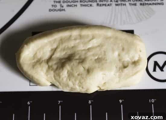 A piece of dough patted flat into an oval shape on a silicone mat with measurements.