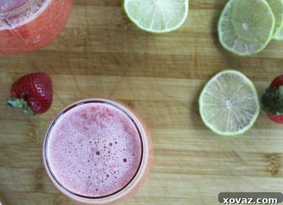 strawberrylimeade1 A close-up shot of the vibrant red strawberry limeade being poured from a blender pitcher into a tall glass, highlighting its smooth texture and rich color.