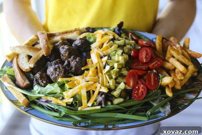Cheeseburger Salad from foodiewithfamily.com with sesame bun croutons. grilled meatballs and green onions, cheese, pickles, tomatoes, and hot fries.