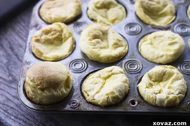 A tray of golden brown, fluffy mini puff pancakes, fresh from the oven, with their centers slightly sunken, ready to be filled.