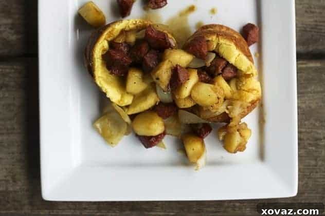 A close-up of a plate featuring Kielbasa, Apple, and Onion Stir-Fry carefully piled onto a stack of mini puff pancakes, showcasing the rich colors and textures.