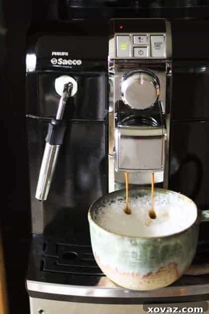 The sleek Philips Saeco Syntia Focus espresso machine brewing a shot, with a Dirty Chai ready beside it.