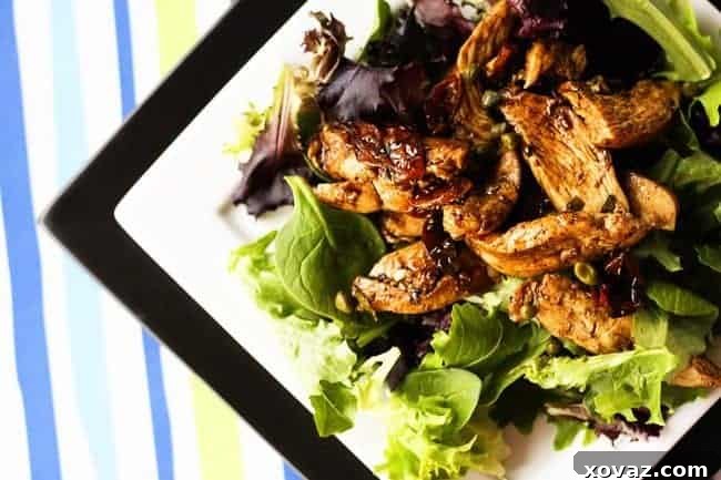 A vibrant, close-up shot of Balsamic Chicken Dinner Salad, featuring tender chicken strips coated in a rich sauce, sun-dried tomatoes, and capers, served over a bed of fresh mixed greens.