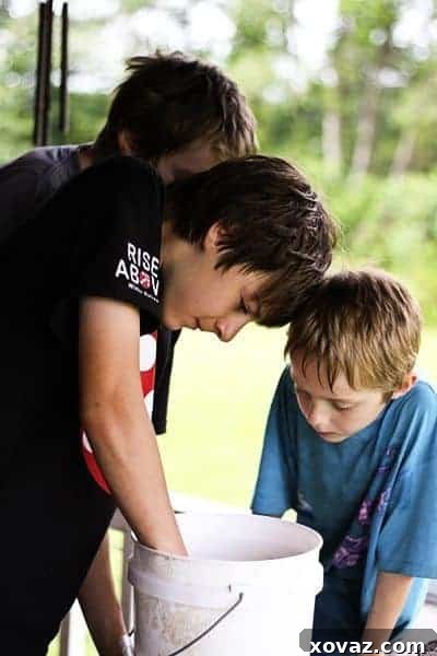 Two joyful young boys stand proudly on a rustic wooden porch, displaying a bucket brimming with lively crawfish they've caught. Their faces beam with pure excitement and the thrill of their summer discovery, illuminated by natural daylight.