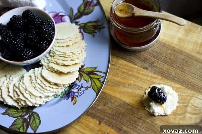 Close-up of a crispbread topped with goat cheese, a fresh blackberry, and a golden honey drizzle, ready to be served as an appetizer.