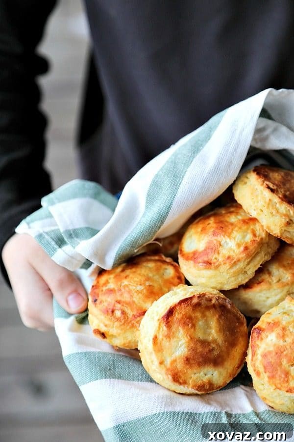 Perfect flaky buttermilk biscuits in green and white towel lined bowl, held by boy in black long sleeved shirt, wooden porch