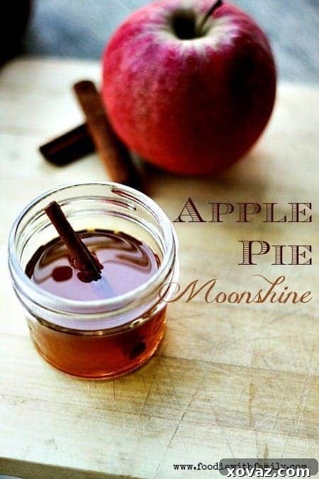 Homemade Apple Pie Moonshine in a mason jar, garnished with cinnamon sticks and apple slices, on a rustic wooden surface.