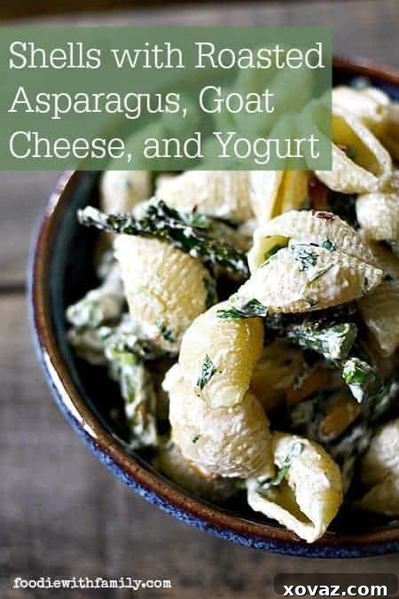 Vertical shot of Shells with Roasted Asparagus, Goat Cheese, and Yogurt, garnished with toasted pine nuts and fresh herbs, highlighting a fresh and appealing spring recipe.