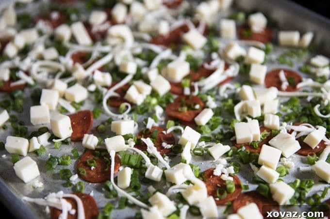 A sheet pan filled with uncooked Pizza Frittata ingredients before baking. Diced mozzarella cheese, green onions, and slices of pepperoni are evenly scattered across the bottom, ready for the whisked egg and cream mixture to be poured over them. The pan is well-greased, hinting at an easy release.