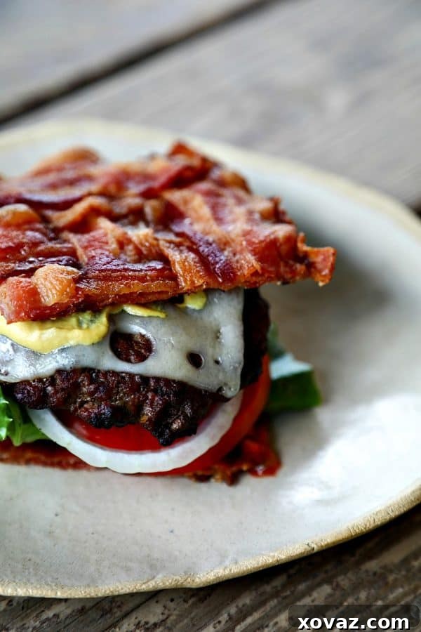 Indulgent Low-Carb Bacon Bun Swiss Burger featuring a crispy, basket-weave bacon bun, melted Swiss cheese, a juicy ground chuck burger, a hint of Dijon mustard, fresh leaf lettuce, ripe tomato, and sweet onion. Perfect for a keto-friendly meal.