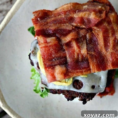 A top-down view of a fully assembled Low-Carb Bacon Bun Swiss Burger, showing the crispy bacon bun, melted Swiss cheese, and fresh ingredients.