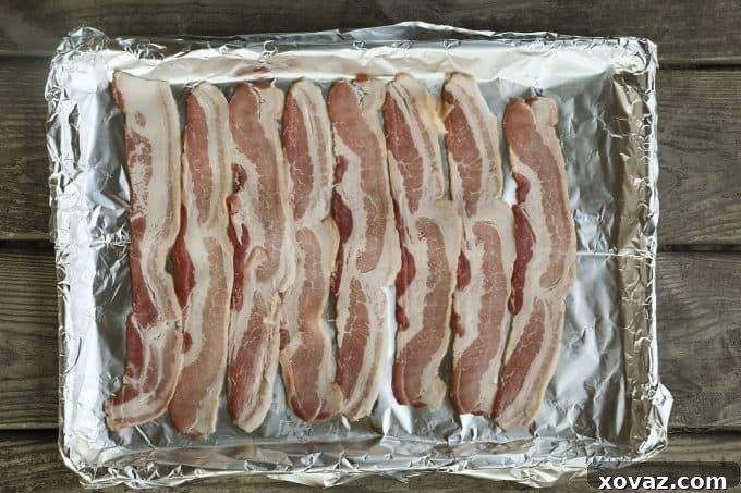 First step in making a Low-Carb Bacon Bun Swiss Burger: Laying out eight slices of Sugardale Hickory Smoked Bacon side-by-side on a foil-lined baking sheet, ready for weaving.