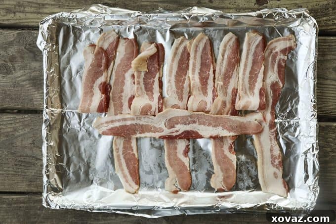 Continuing the bacon weave for the Low-Carb Bacon Bun Swiss Burger: One slice of bacon is laid perpendicularly across the folded-back strips, forming the initial interlocking pattern.