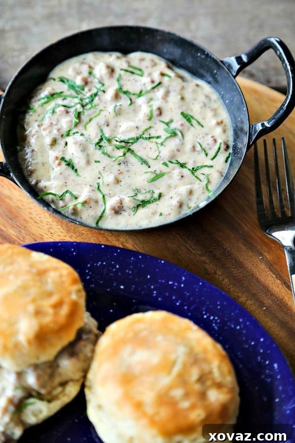 A bowl of Classic Sausage Gravy, rich and creamy, served alongside golden-brown, flaky buttermilk biscuits on a rustic wooden board, evoking warmth and comfort.
