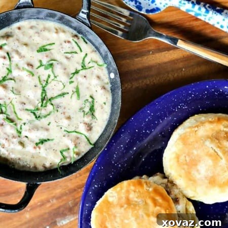 Classic Sausage Gravy in black and white enameled bowl with handles, biscuits on blue and white enamel plate, round wooden platter, fork with wooden handle, blue and white enamel metal spoon