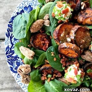 Melting Sweet Potato Salad, baby spinach, caramelized roasted sweet potatoes, maple candied pecans, crumbled bacon, goat cheese with herbs and bacon, chopped chives, on an antique blue and white plate.