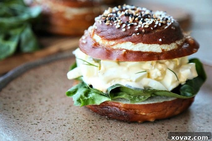 Dill Pickle Egg Salad on lettuce and pretzel roll, brown speckled pottery plate, lettuce leaves, wooden cutting board, rustic wood table, close up