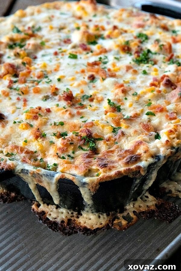 Close-up of a spoon scooping creamy hot corn dip, highlighting the textures of sweet corn, chicken, bacon, Hatch chiles, and melted cheese, perfect for a gathering.