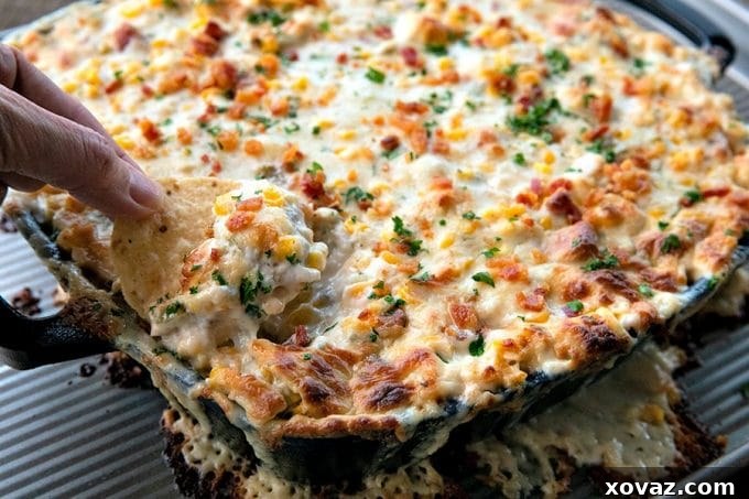 Overhead view of a vibrant hot corn dip, featuring chunks of chicken, crispy bacon, green onions, and sweet corn in a creamy, cheesy sauce, served in a rustic dish.