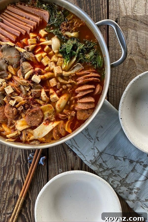 Budae Jjigae Korean Spicy Sausage Stew 2 Korean Army Stew in a stainless steel pan with two empty bowls, chopsticks, and a blue linen.