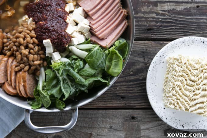 Budae Jjigae Korean Spicy Sausage Stew 4 Budae Jjigae or Korean Army Stew ready to simmer. Stainless steel everyday pan filled with bok choy, sliced sausace, spam, mushrooms, tofu cubes, baked beans, and sauce. Ramen noodles on a plate next to the pan.