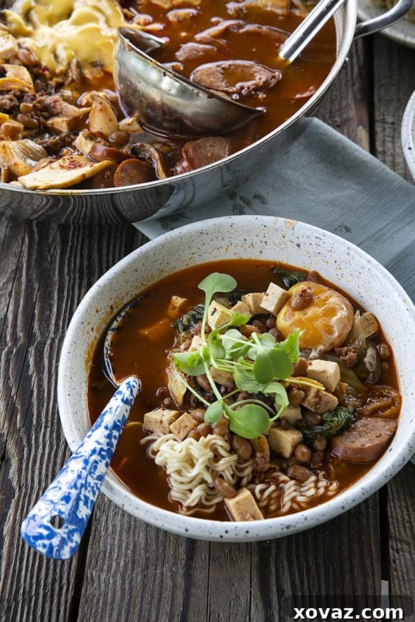 Budae Jjigae Korean Spicy Sausage Stew 6 Korean Army Stew or Budae Jjigae in a white bowl with an egg yolk and a blue enamel spoon.