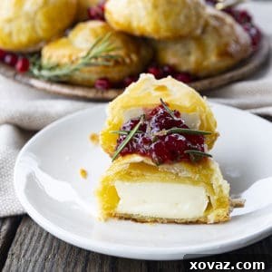 Bite-sized baked brie in puff pastry with rosemary, pomegranate seeds, and sweet and spicy cranberry sauce.