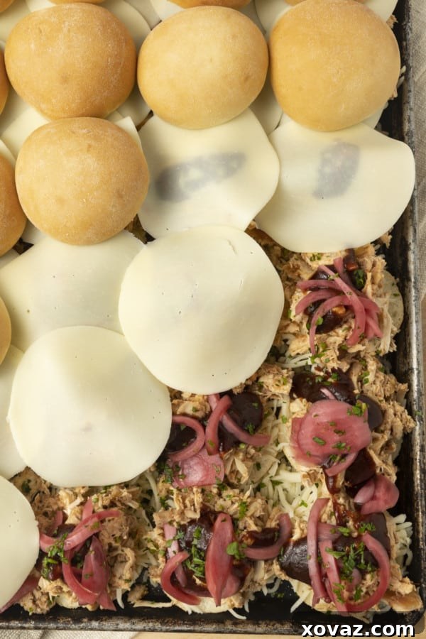 A tantalizing close-up of a single BBQ Chicken Slider, featuring a golden Rhodes roll, shredded chicken, melted provolone, and visible pickled onions, ready to be devoured.