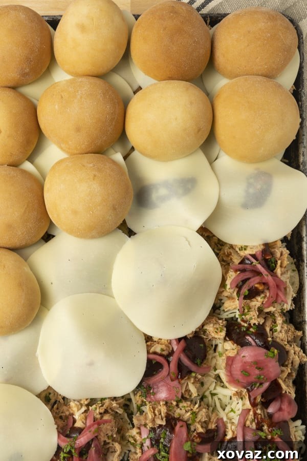 The assembled bottom halves of BBQ Chicken Sliders, layered with saucy shredded chicken and thinly sliced pickled red onions, ready for the cheese and top buns.