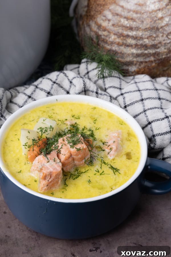 A pot of Finnish Salmon Soup simmering on the stove, with a creamy broth and chunks of salmon, potatoes, and dill.