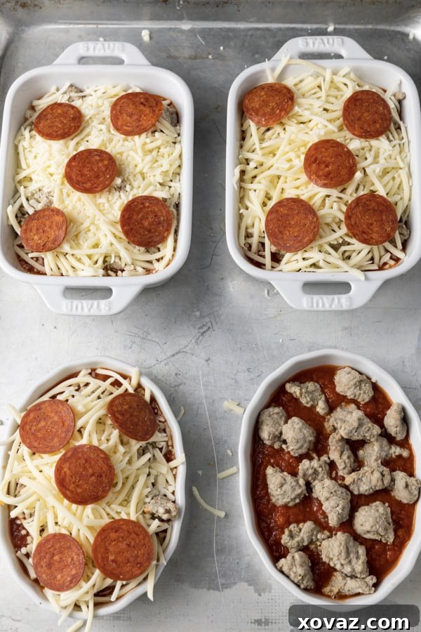 The initial layer of marinara sauce and Italian sausage crumbles in individual oven-safe bowls, before adding cheese and pepperoni.