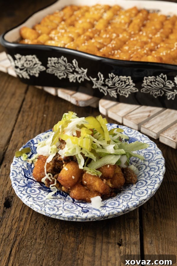 A dish of Big Mac Tater Tot Casserole, hot out of the oven, with bubbly cheese and crispy tots, garnished with fresh lettuce, pickles, and onions.