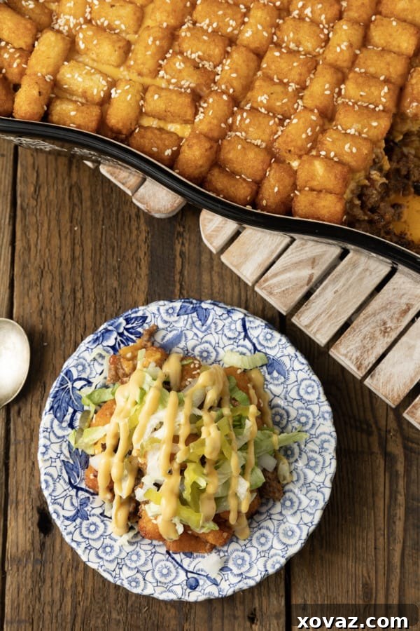 A large serving of Big Mac Tater Tot Casserole, topped with fresh lettuce, diced pickles, onions, and a drizzle of special sauce, ready to be enjoyed.