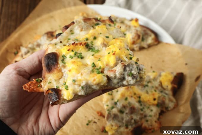 Close-up shot of a slice of Sausage Gravy Breakfast Pizza with melted cheese, fluffy scrambled eggs, and rich gravy, ready to be enjoyed.