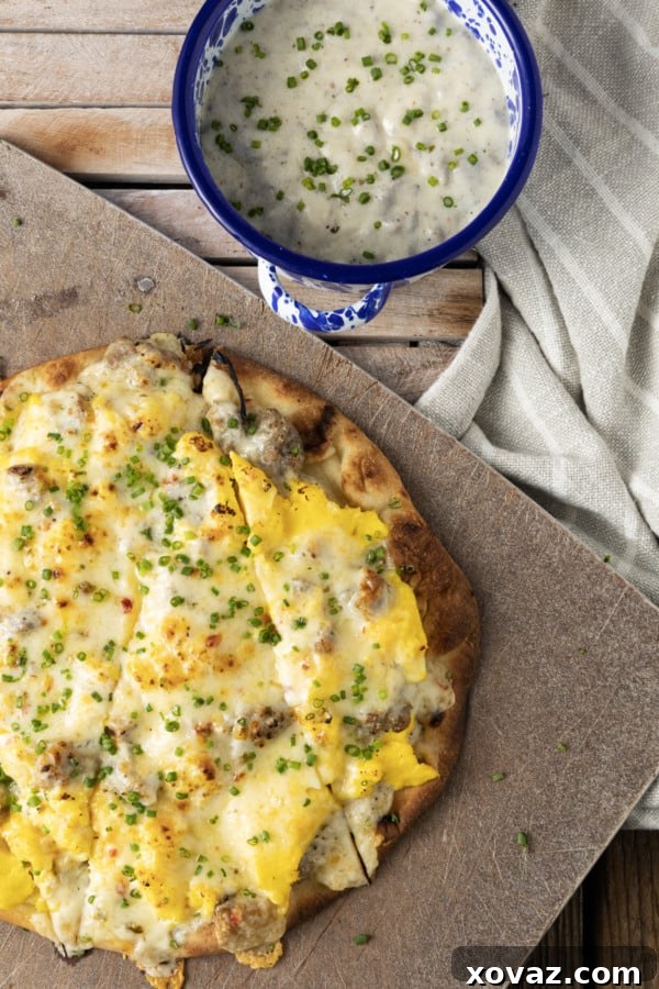 Overhead view of an unbaked Sausage Gravy Breakfast Pizza, highlighting the rich, creamy sausage gravy spread over fluffy eggs and crust.